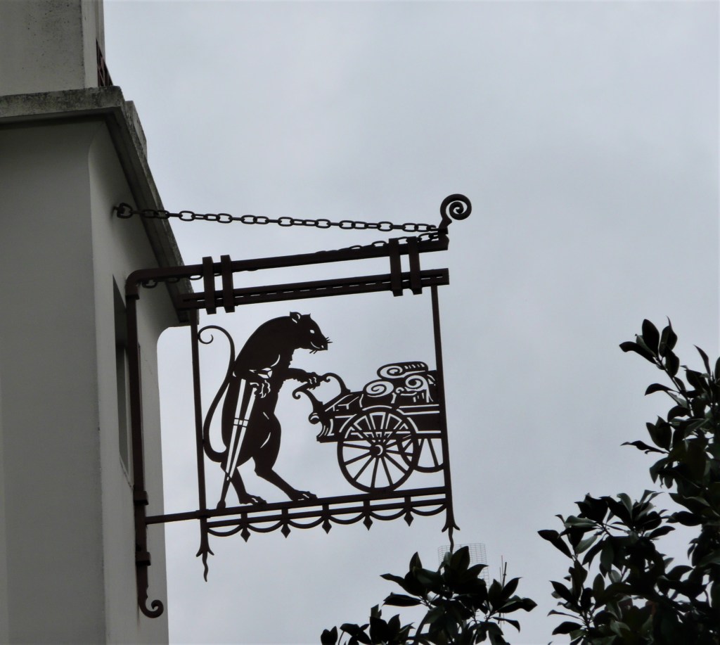 Die Ratte mit Krücke ist mir bis heute ein Rätsel... Dieses Schild hängt auf Höhe des 3. Stocks eines Art-Déco-Hauses in der Altstadt von Nantes. Was wird hier gehandelt oder betrieben?